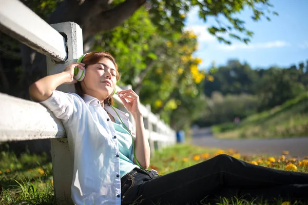 Młode kobiety leżące w trawie lato ze słuchawkami, słuchanie muzyki i relaksujące, 2017 odcień zieleni — Zdjęcie stockowe