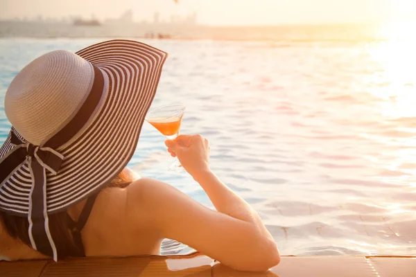 Jovem mulher de chapéu grande relaxante na piscina, perto do mar ao pôr do sol — Fotografia de Stock