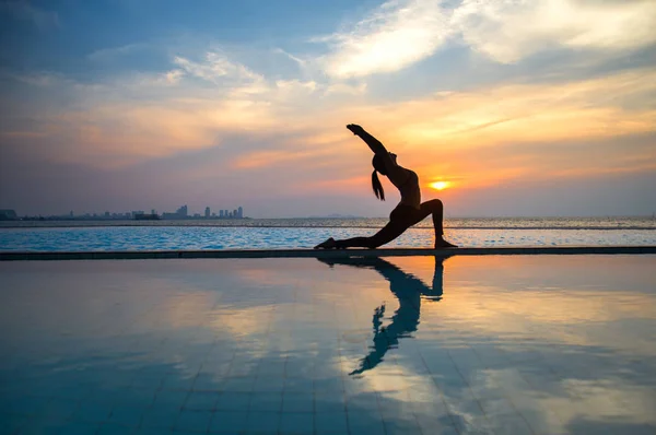 Силуэт молодая женщина практикует йогу на бассейне и на пляже на закате . — стоковое фото