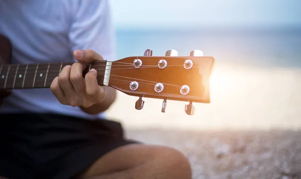 Cerca de hombre guapo tocando la guitarra clásica sentado en la playa en vacaciones — Foto de Stock