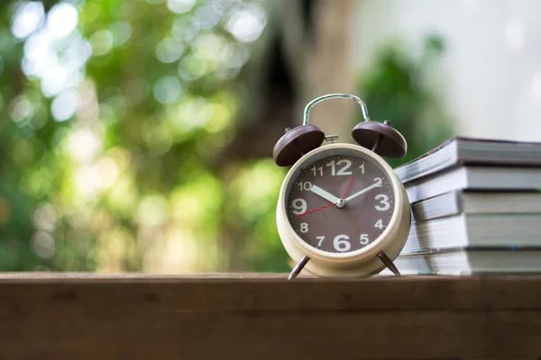 Relógio de alarme retrô apontando às 10: 00 horas com livro ou memorando na mesa de madeira . — Fotografia de Stock