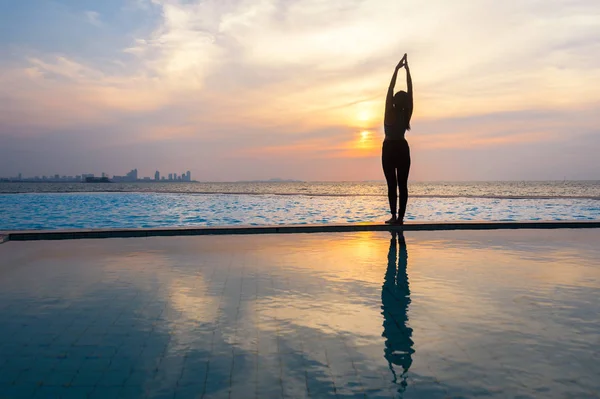 Silhouette jeune femme pratiquant le yoga sur la piscine et la plage au coucher du soleil . — Photo