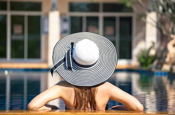Jovem mulher de chapéu grande relaxante na piscina, verão — Fotografia de Stock
