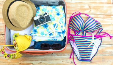 Çantayı turistik şeyler ile açın: kadın şapka, Mayo, kamera, kot şort, elbiseler, güneş gözlüğü, parfüm, tablet ahşap arka plan üzerinde