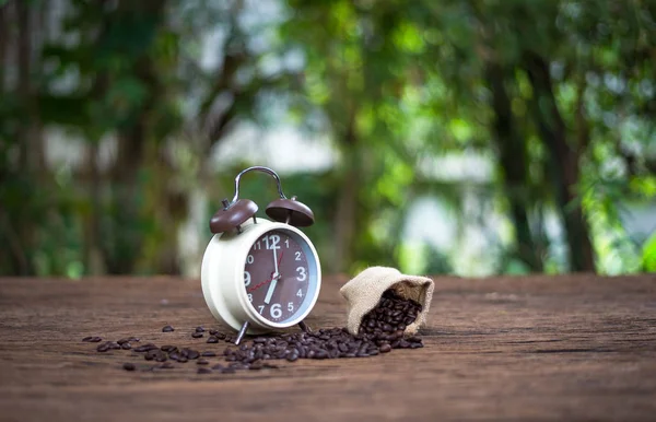 Reloj despertador con granos de café en mesa de madera con luz de la mañana, concepto Start up — Foto de Stock
