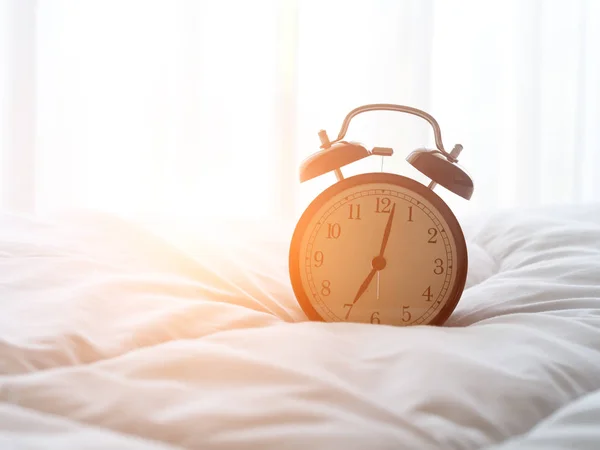 Reloj despertador en la cama por la mañana con luz solar — Foto de Stock