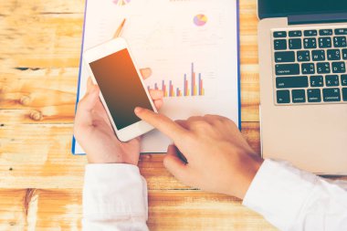 Genç adam akıllı telefon ve dizüstü bilgisayar, iç, onun işyerinde teknolojisini kullanarak adam akıllı telefon kullanarak adamın ellerini kullanarak evden çalışma