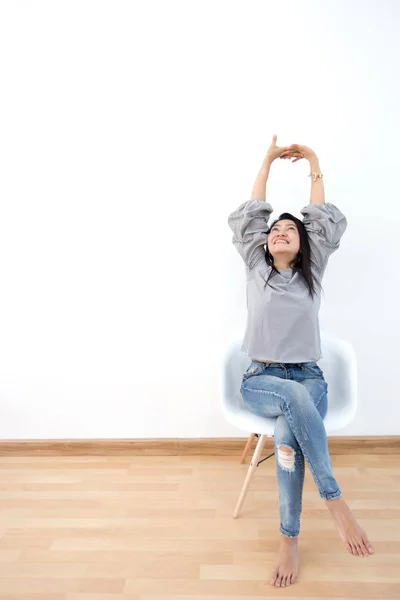 Ελκυστική ασιατική κορίτσι κάθεται σε λευκό μοντέρνα καρέκλα και να χαλαρώσετε στο σπίτι — Φωτογραφία Αρχείου
