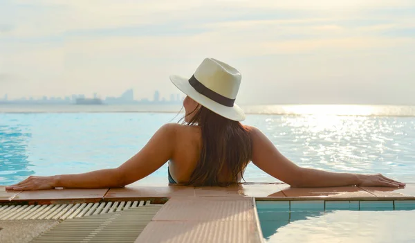 Mulher de chapéu grande relaxante na piscina, perto do mar ao pôr do sol — Fotografia de Stock