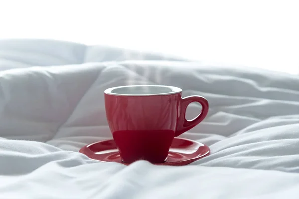 Frischer Morgenkaffee in roter Tasse auf dem Bett — Stockfoto