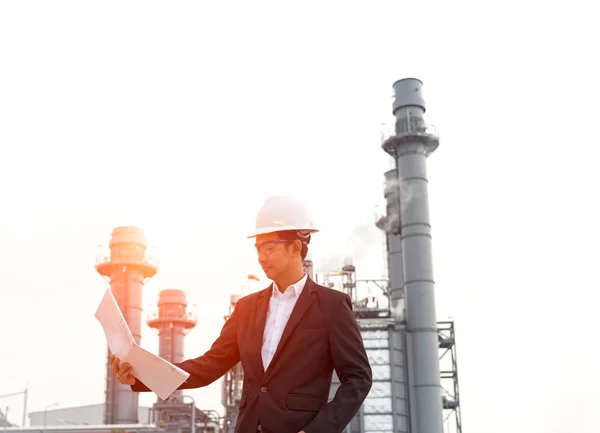 Engenheiro usando capacete branco segurando desenho de papel com fundo de refinaria de óleo . — Fotografia de Stock