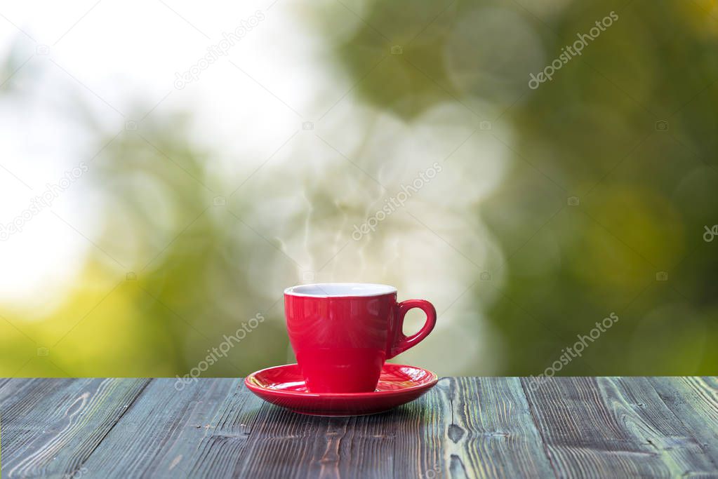 Hot coffee with in red cup on wood table and nature bokeh background