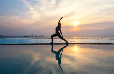 Pratik Yoga Yüzme Havuzu ve deniz üzerinde günbatımında siluet genç kadın.