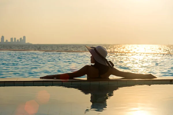 在游泳池边，在夕阳海边放松的大帽子的女人 — 图库照片