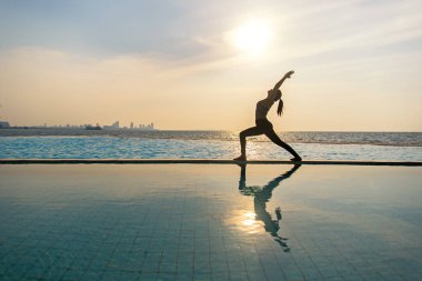 Pratik Yoga Yüzme Havuzu ve deniz üzerinde günbatımında siluet genç kadın.