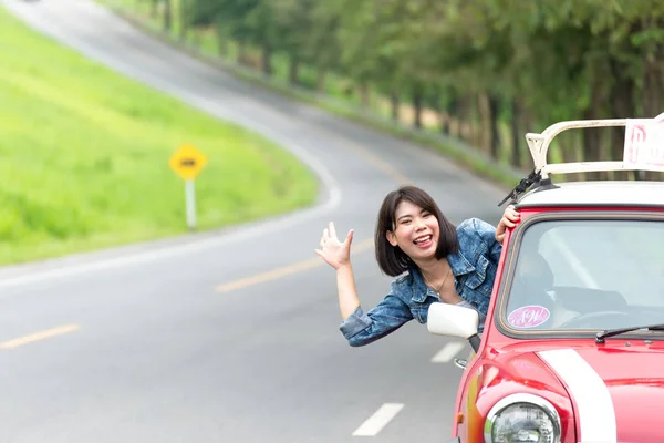 Woman in car road trip waving out the window smiling
