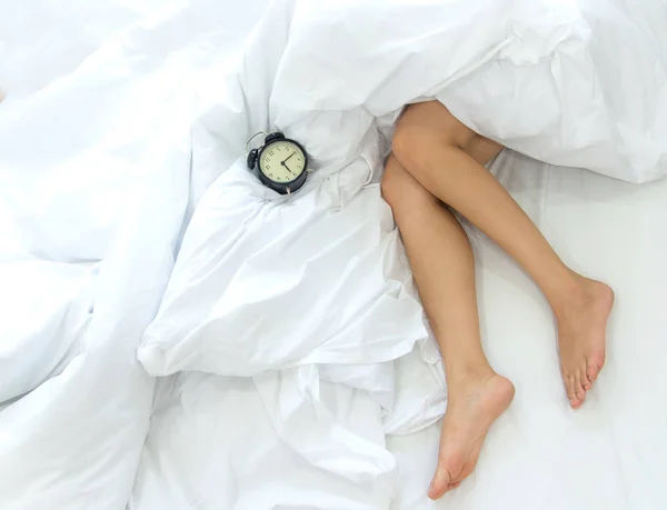 Closeup of sexy female legs with alarm clock on the bed. Woman lazy girl relaxing lazing in bedroom — Stock Photo, Image