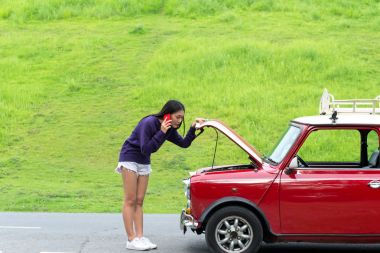 Sokakta bozuk arabaya bakarken cep telefonu kullanan genç bir kadın.