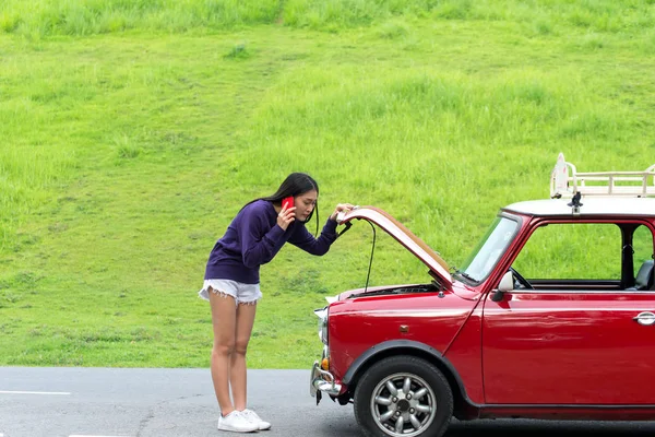 Mujer joven usando el teléfono móvil mientras mira el coche roto en la calle — Foto de Stock