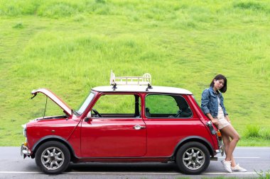 Sokakta bozuk arabaya bakarken cep telefonu kullanan genç bir kadın.