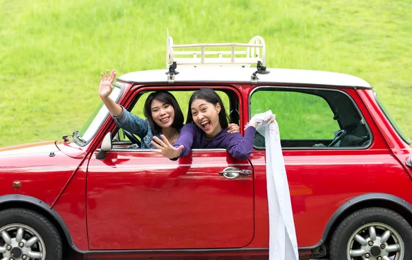 Two travel woman in car road trip waving out the window smiling — Stock Photo, Image