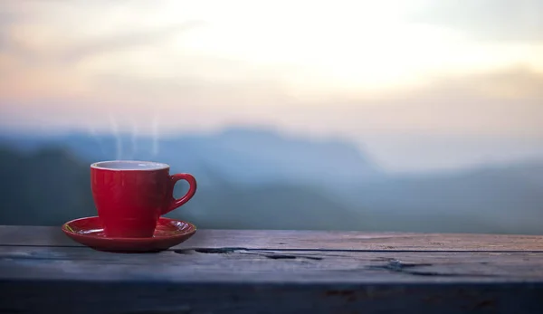 Gelas merah dengan kopi di atas meja di atas pegunungan dengan sinar matahari. Latar belakang alam kecantikan — Stok Foto