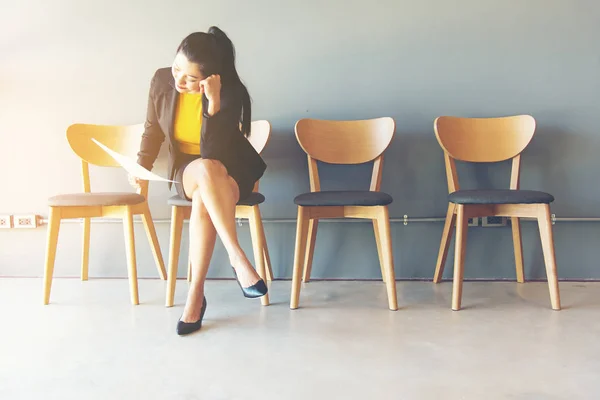 Cansado de esperar. Empresaria sosteniendo papel y mirando hacia otro lado mientras está sentada sobre una silla sobre un fondo gris — Foto de Stock