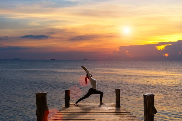 Meditação menina no mar durante o pôr do sol na madeira a ponte. Sílhueta de ioga. Fitness e estilo de vida saudável . — Fotografia de Stock