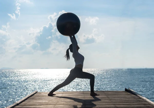 瑜伽球，普拉提球在海滩日出背景的年轻女子 — 图库照片