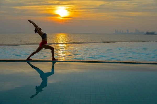 剪影上练瑜伽的游泳池和海滩日落时分的年轻女人。健康概念. — 图库照片