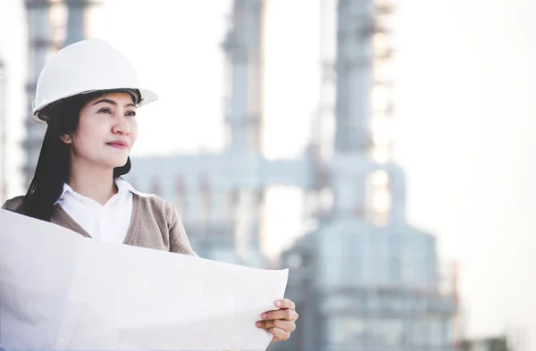 Ingeniero mujer asiática con sombrero duro sosteniendo papel de impresión azul mirando hacia otro lado inspeccionando el progreso en el sitio de la planta de energía de construcción, control de seguridad. Concepto de Ingeniero . —  Fotos de Stock