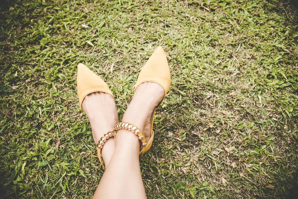 Piernas con zapatos de tacón alto de moda amarillo sobre hierba verde con espacio de copia. Un tono vintage. Concepto de estilo de vida . — Foto de Stock