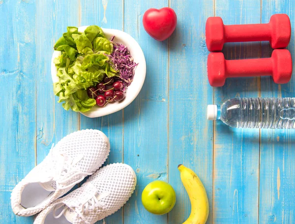 Sağlıklı yaşam spor ekipmanları fitness, spor ayakkabı, yeşil elma, tatlı su ve sağlıklı gıda mavi ahşap zemin üzerinde. Sağlıklı kavramı.