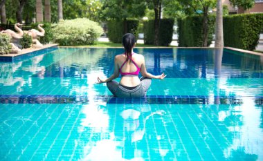 Asia woman doing yoga fitness exercise for relax and healthy beside swimming pool background.  Healthy Concept clipart