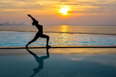 Pratik Yoga Yüzme Havuzu ve deniz üzerinde günbatımında siluet genç kadın. Sağlıklı kavramı.