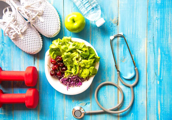 Sağlıklı yaşam spor ekipmanları fitness, spor ayakkabı, yeşil elma, tatlı su ve sağlıklı gıda mavi ahşap zemin üzerinde. Sağlıklı kavramı.