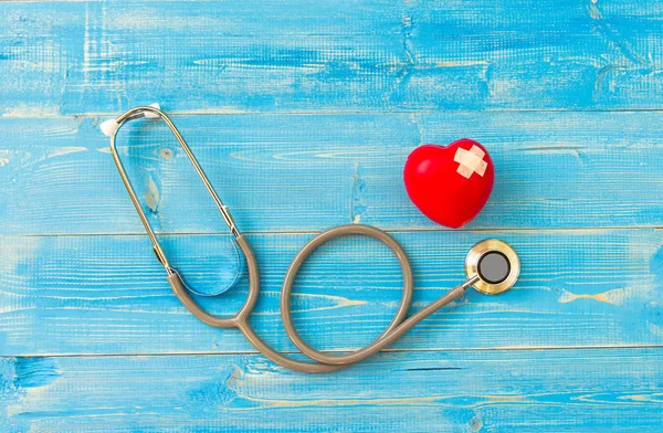 Un solo corazón rojo amor forma bola de ejercicio mano sola con vendaje MD médico médico estetoscopio fondo de madera azul. Concepto saludable — Foto de Stock