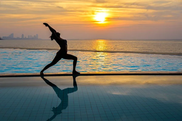 Pratik Yoga Yüzme Havuzu ve deniz üzerinde günbatımında siluet genç kadın. Sağlıklı kavramı.