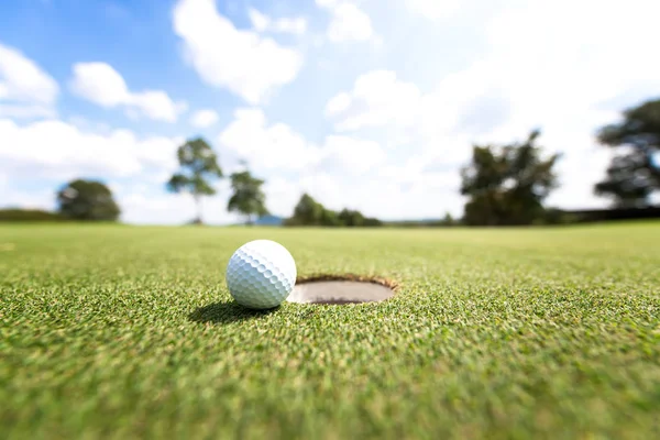 Bola de golfe perto do buraco, fundo céu azul — Fotografia de Stock