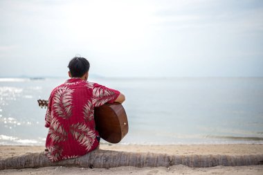 Yakışıklı adam sahilde tatil içinde oturan klasik gitar çalmak. Yaz konsepti