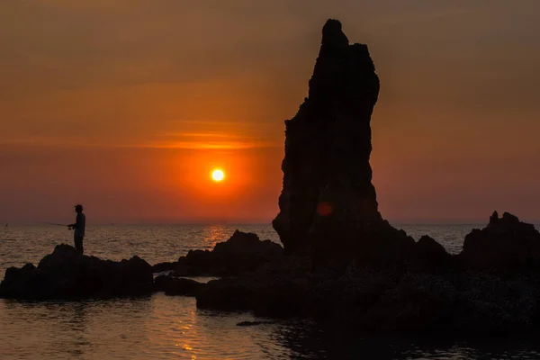 Kayaların üzerinde günbatımında ayakta balıkçılar — Stok fotoğraf