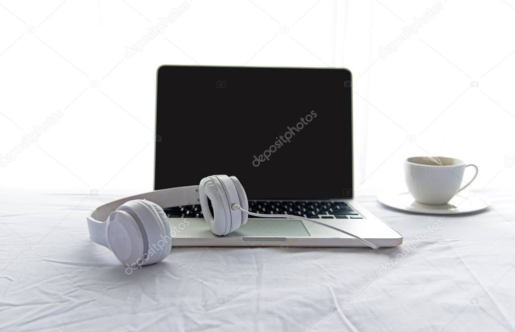 Morning music background. Coffee with laptop in white bed, sheet, duvet and pillow, messed up. Music and Lifestyle Concept.