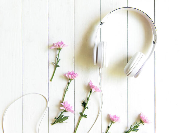 Top view headphones on white desk with pink flower and copyspace area for a text. Music and lifestyle Concept