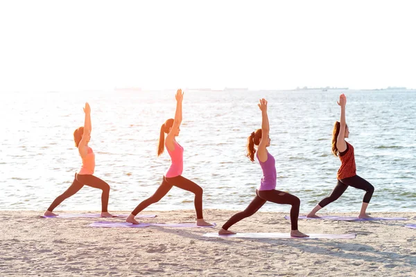 Asya insanlar grup yapma savaşçı poz üzerinde plaj, fitness, spor, yoga ve sağlıklı bir yaşam tarzı. Sağlıklı kavramı