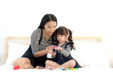 Asya genç anne ve küçük kızı beyaz yatakta renkli oyuncak kil ile oynarken. Yaşam tarzı kavramı