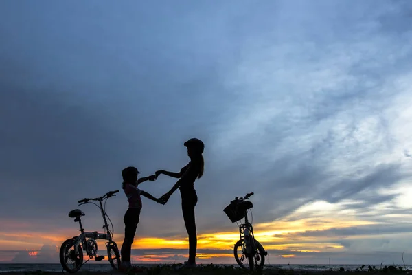 Sylwetka biker piękne rodziny o zachodzie słońca nad oceanem. Mama i Córka, jazda na rowerze na plaży. Koncepcja życia. — Zdjęcie stockowe