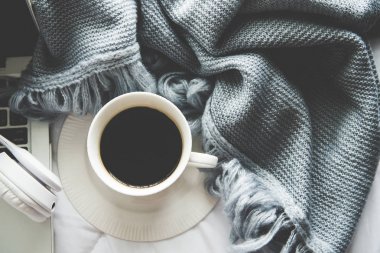 Beyaz yatak ve kahve hatmi, güneşli günde sıcak örme kazak ile dizüstü bilgisayar çalışma ve dinle müzik. Sıcacık kış eve sabah tatil. Müzik ve yaşam tarzı kavramı. 
