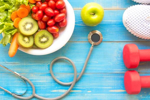 Diet and weight loss for healthy care with medical stethoscope, fitness equipment,measuring tap,fresh water and green apple on wooden background top view.