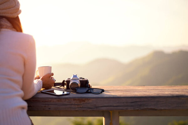 Smiling asian Woman drinking coffee and tea and take a photo and relax in sun sitting outdoor in sunshine light enjoying her warm morning at balcony house, vintage. Lifestyle Concept.