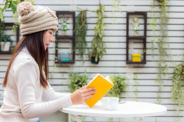 アジアの若い女性のセーターを着て 座っていると読書と本ホット コーヒーで冬の庭を家します ライフ スタイルのコンセプト — ストック写真
